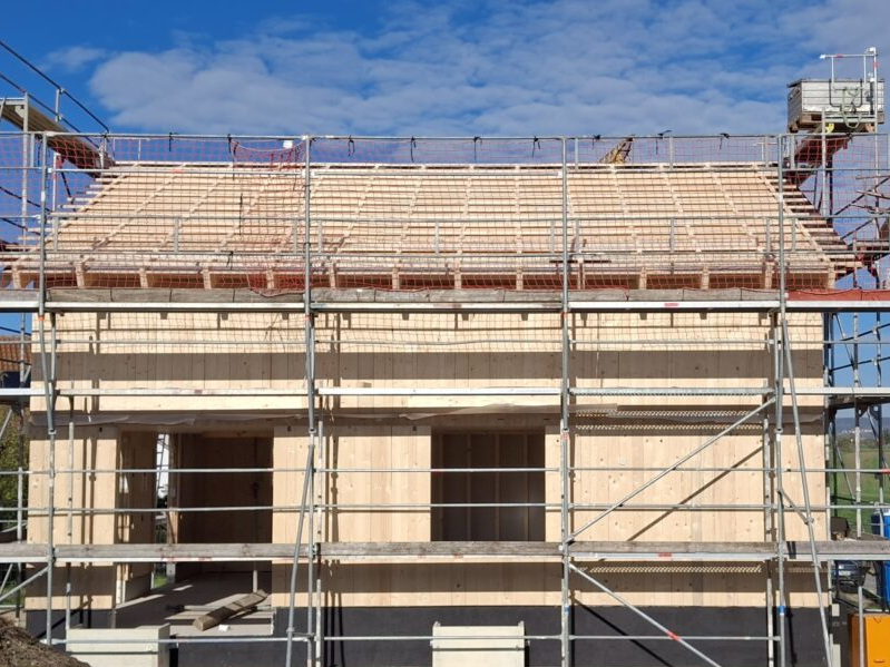 Neubau eines Holzhauses mit Gerüst und Dachkonstruktion unter blauem Himmel.