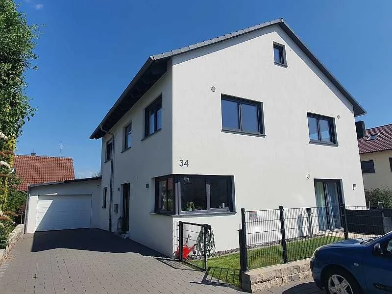 Modernes weißes Einfamilienhaus mit Garage, Zaun und Garten bei Sonne