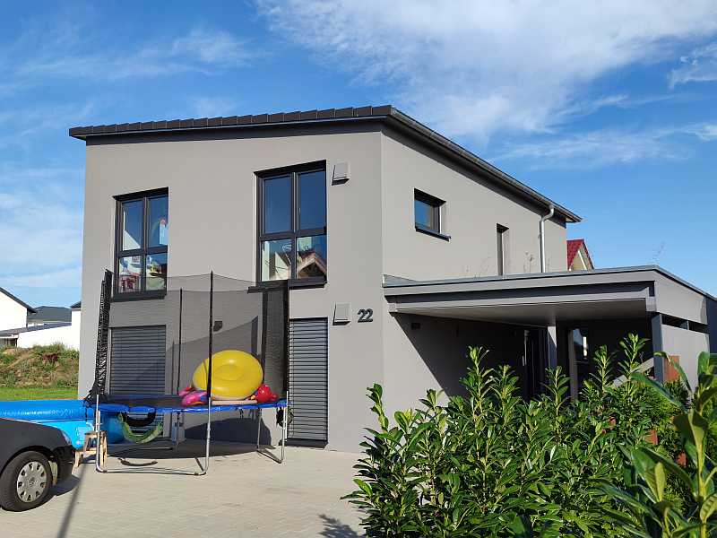 Modernes Einfamilienhaus mit Flachdach, Garten, Carport und Trampolin im Vorgarten.